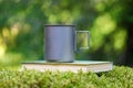 Titanium mug on a book in the forest. Fern and moss background is blurred