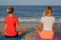 Young women practicing yoga on the beach at sunset. Girls meditating, sitting in lotus pose Royalty Free Stock Photo