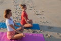 Young women practicing yoga on the beach at sunset. Girls meditating, sitting in lotus pose Royalty Free Stock Photo