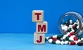 TMJ word on cubes on a blue background with a jar of tablets