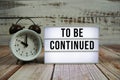 To be Continued text on light box with alarm clock on wooden background Royalty Free Stock Photo