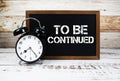 To Be Continued text message and alarm clock on wooden background Royalty Free Stock Photo