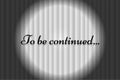 To be continued text on white closed silky luxury theater curtain background with spotlight beam illuminated. Black