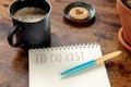 To do list with coffee and a cookie, a notebook and a blue pen on a wooden desk