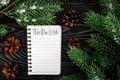 To do list for winter shopping at notebook near spruce branch and pinecones on grey wooden background top view Royalty Free Stock Photo