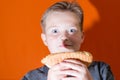 To eat or not to eat trash food.confused young kid,boy holding hot dog over carrot background.closeup Royalty Free Stock Photo