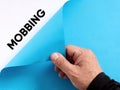 To uncover mobbing in the business workplace or school concept. Male hand opens the blue paper and reveals the word mobbing