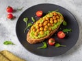 Toast with avocado, roasted chickpeas, cherry tomatoes, herbs on a dark plate. Royalty Free Stock Photo