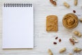 Toast, bowl of peanut butter, peanuts and notebook on a white wooden background, top view. Royalty Free Stock Photo