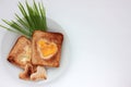 Toast bread with fried egg in a heart shaped hole and greens on plate on white background.