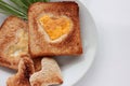 Toast bread with fried egg in a heart shaped hole and greens on plate on white background.