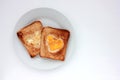 Toast bread with fried egg in a heart shaped hole on plate on white background. Creative Valentine\'s day