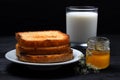 Toast on a plate with milk and a can of honey. On a black wooden background