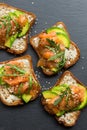 Toast sandwich with butter, avocado and salmon, decorated with arugula and sesame seeds, on a black stone board Royalty Free Stock Photo