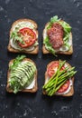 Toast sandwiches with avocado, salami, asparagus, tomatoes and soft cheese on dark background, top view. Tasty breakfast, snack or Royalty Free Stock Photo