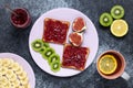 Toast sandwiches with raspberry jam, top view. Red confiture spread on a slice of white bread. Tea with lemon and fresh fruits on