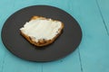 Toast slice with creme cheese on a black plate, on a blue table ,side view close up