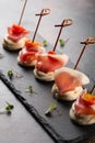 Toasted canape with bacon, tomatoes cherry and cream cheese on black board at dark background close-up