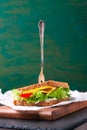 Toasted sandwich with salad leaves, tomatoes and cheese with fork on a cutting board on a dark background Royalty Free Stock Photo