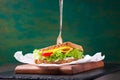 Toasted sandwich with salad leaves, tomatoes and cheese with fork on a cutting board on a green background Royalty Free Stock Photo