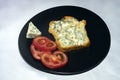 Toasted slice of bread with gorgonzola moldy cheese and tomato slices, o a black ceramic plate Royalty Free Stock Photo