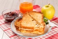 Toasted slices of bread with cheese and green parsley on white plate, glass of orange juice, apple and bowl with strawberry jam