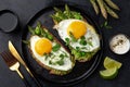 Toasts with avocado, asparagus and fried egg on black plate