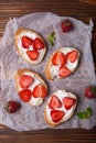 Toasts or bruschetta with strawberries on cream cheese on wooden background.