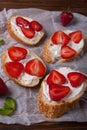 Toasts or bruschetta with strawberries on cream cheese on wooden background.