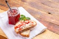 Toasts with curd and jam and glass jar of strawberry jam on white towel on rustic wooden table