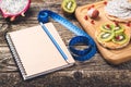 Toasts with fruit, measuring tape and empty notebook on wooden background. Slimming plan with fruits. Planning healthy diet