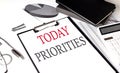 TODAY PRIORITIES text on paper clipboard with chart and notebook on withe background
