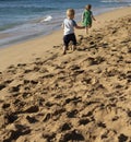 Two young children, a boy and a girl, play together on a beach with the ocean in the background