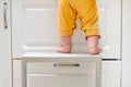 Toddler baby boy climbed with his feet on a high chair to climb on the kitchen cabinet. Child safety issues in the home room, Royalty Free Stock Photo