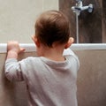 Toddler baby boy climbs into the white tub standing at the edge. Child plays in the bathroom, kid and bath Royalty Free Stock Photo