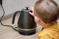 Toddler baby boy holds a hot kettle with boiling water. Child safety issues in the home room, little kid Royalty Free Stock Photo