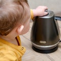 Toddler baby boy holds a hot kettle with boiling water. Child safety issues in the home room, little kid Royalty Free Stock Photo