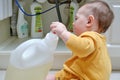 Toddler baby boy is playing with detergents and cleaning products in an open kitchen cabinet. Child safety issues in the home room Royalty Free Stock Photo