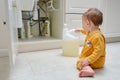 Toddler baby boy is playing with detergents and cleaning products in an open kitchen cabinet. Child safety issues in the home room Royalty Free Stock Photo