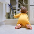 Toddler baby boy is playing with detergents and cleaning products in an open kitchen cabinet. Child safety issues in the home room Royalty Free Stock Photo