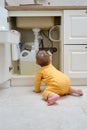 Toddler baby boy is playing with detergents and cleaning products in an open kitchen cabinet. Child safety issues in the home room Royalty Free Stock Photo