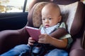 Toddler baby boy sitting in car seat and watching a video from smart phone