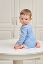 Toddler baby climbed on the kitchen white table. A child in danger clim Royalty Free Stock Photo