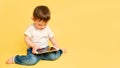 Toddler baby with a digital tablet on a studio yellow background. Happ