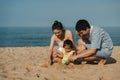 toddler baby girl playing sand toy with father and mother. happy family on the sea beach Royalty Free Stock Photo