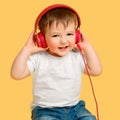 Toddler baby listens to music in red headphones on a studio yellow ba