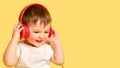 Toddler baby listens to music in red headphones on a studio yellow ba Royalty Free Stock Photo