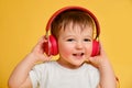 Toddler baby listens to music in red headphones on a studio yellow background. Happy child in a white t-shirt and blue jeans