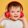 Toddler baby listens to music in red headphones on a studio yellow ba Royalty Free Stock Photo