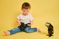 Toddler baby photographer with a camera Canon on a studio yellow ba-